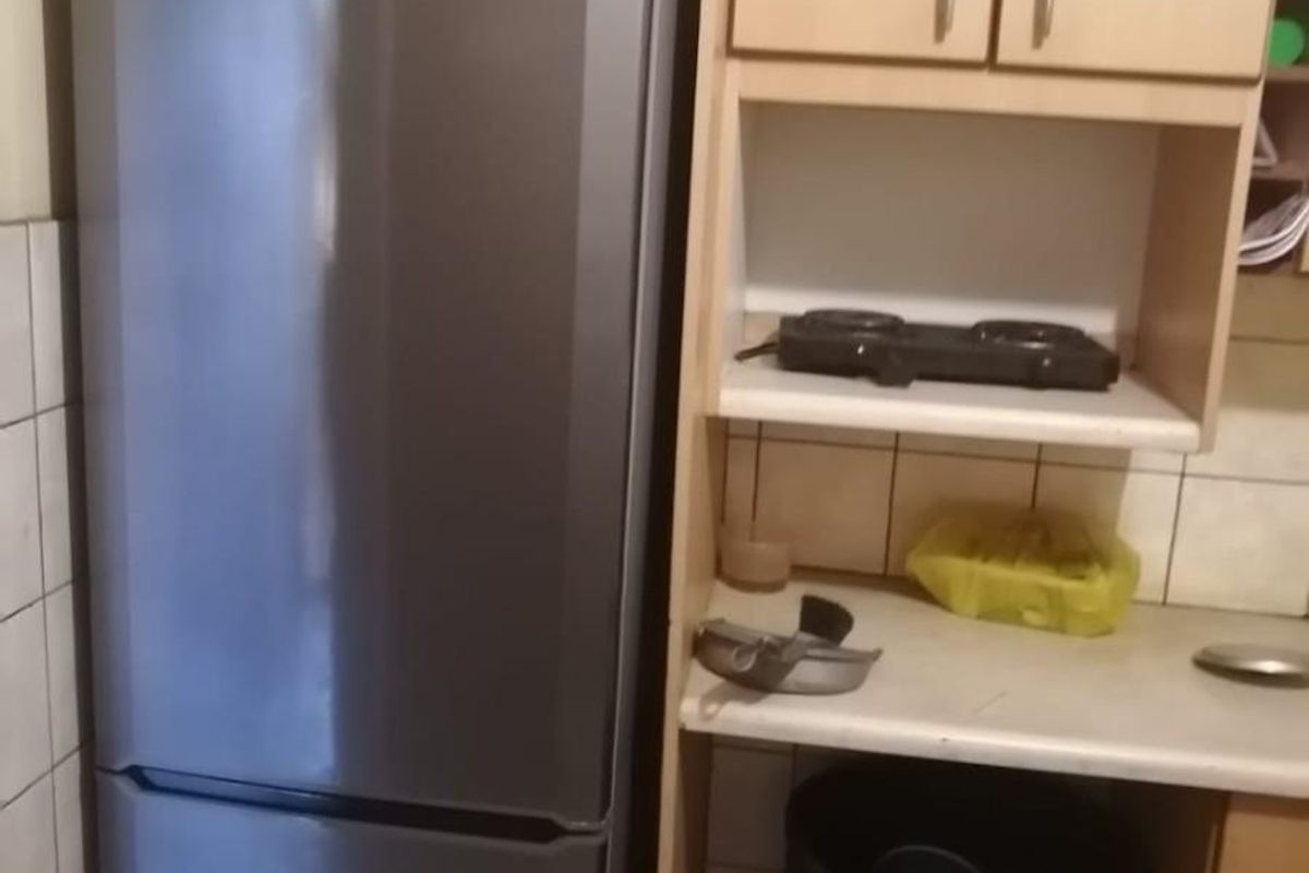 A compact kitchen area featuring light wood-tone cabinetry, tiled splashbacks, and a dedicated space for a refrigerator.