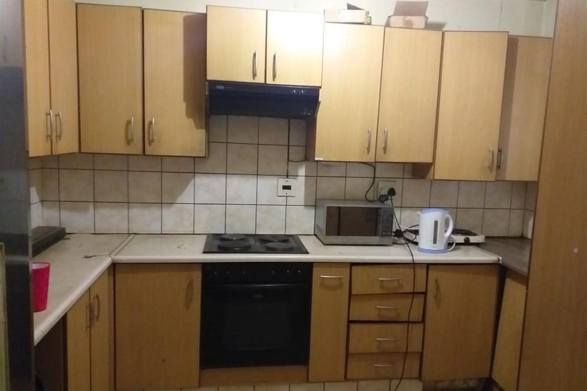 A compact kitchen featuring light wood-tone cabinetry, a built-in electric oven and hob, extractor fan, and tiled splashback.