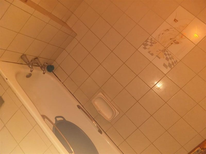 A dated bathroom featuring a standard bathtub with wall-mounted taps and tiled surround, requiring cosmetic updates to modernize the space.