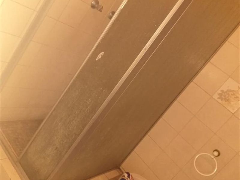 A dated bathroom featuring a shower enclosure with a framed glass screen and standard ceramic wall and floor tiling.