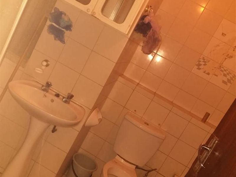 A dated bathroom featuring a pedestal sink, toilet, and wall-mounted medicine cabinet with tiled walls and flooring.