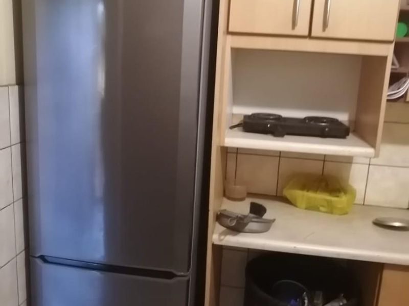 A compact kitchen area featuring light wood-tone cabinetry, tiled splashbacks, and a dedicated space for a refrigerator.