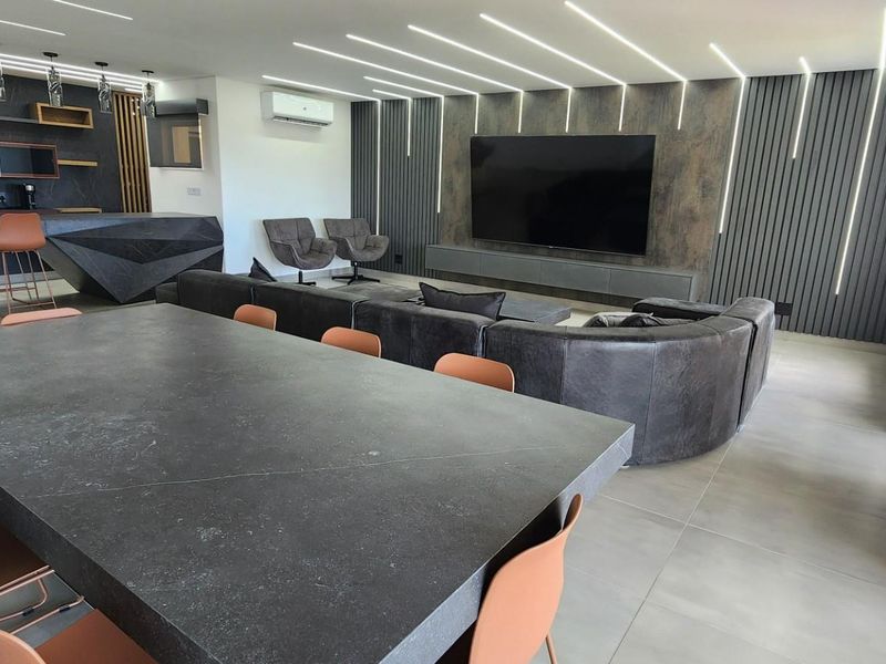 Modern open-plan living area featuring a sleek kitchen with breakfast bar, integrated lighting, and a contemporary media wall with feature paneling.
