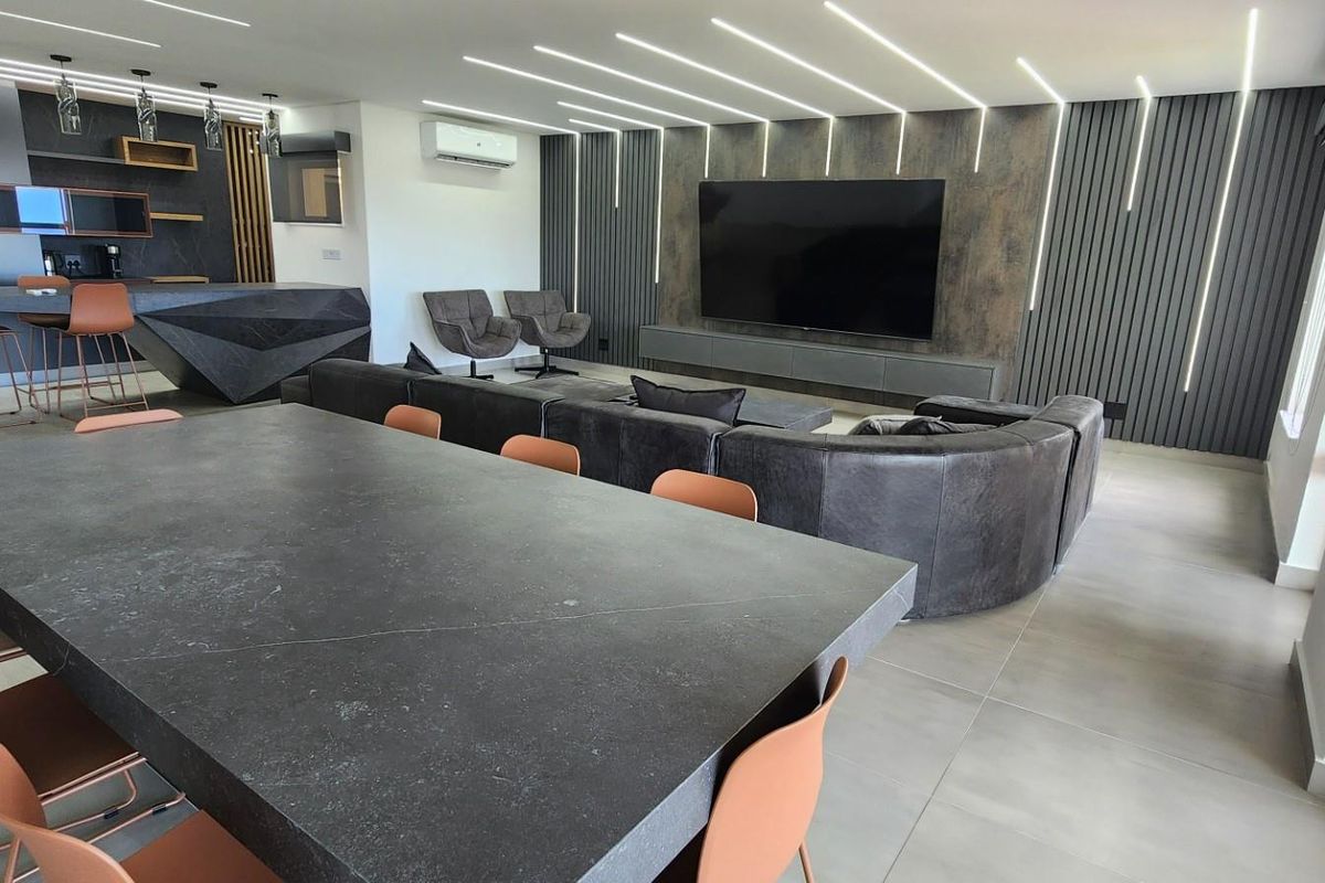 Modern open-plan living area featuring a sleek kitchen with breakfast bar, integrated lighting, and a contemporary media wall with feature paneling.