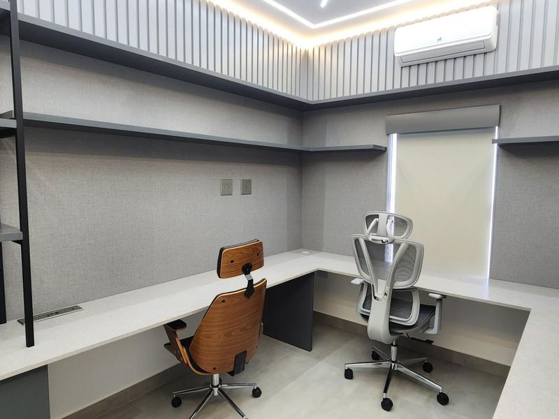 A modern, well-appointed home office featuring custom built-in L-shaped desk, integrated shelving, recessed ceiling lighting, and a wall-mounted air conditioning unit.