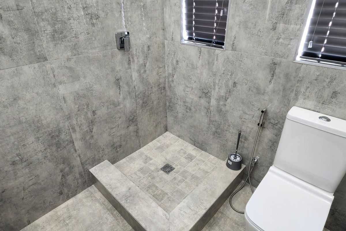 Modern bathroom featuring a walk-in shower with grey textured tiling, a wall-mounted shower mixer, and a contemporary toilet.