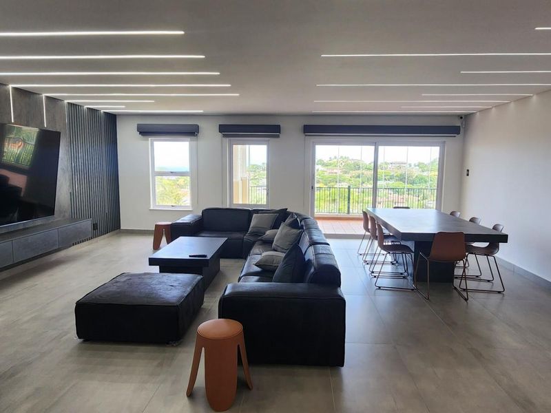 Spacious open-plan living and dining area featuring modern recessed linear ceiling lighting, large-format floor tiles, and sliding glass doors leading to a balcony.