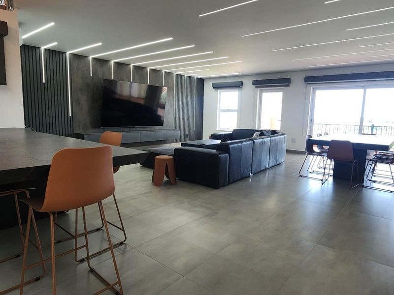 Spacious open-plan living and dining area featuring modern recessed linear ceiling lighting, large format floor tiles, and direct access to a private balcony.