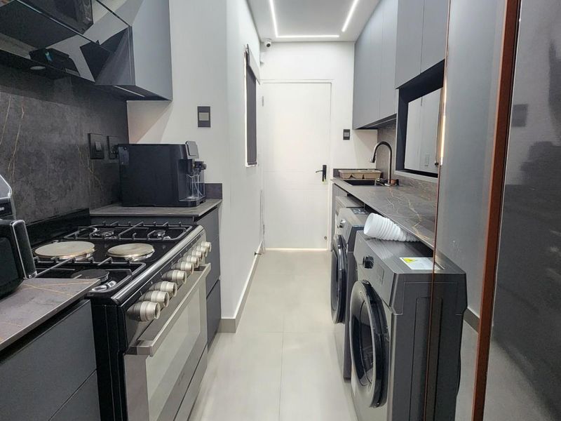 Modern scullery featuring sleek dark cabinetry, stone-look countertops, integrated gas stove, and dedicated laundry appliance connections in a compact, efficient layout.