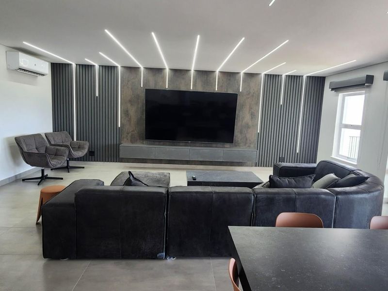 Modern open-plan living area featuring a striking feature wall with integrated LED lighting, sleek cabinetry, and large-format floor tiles.