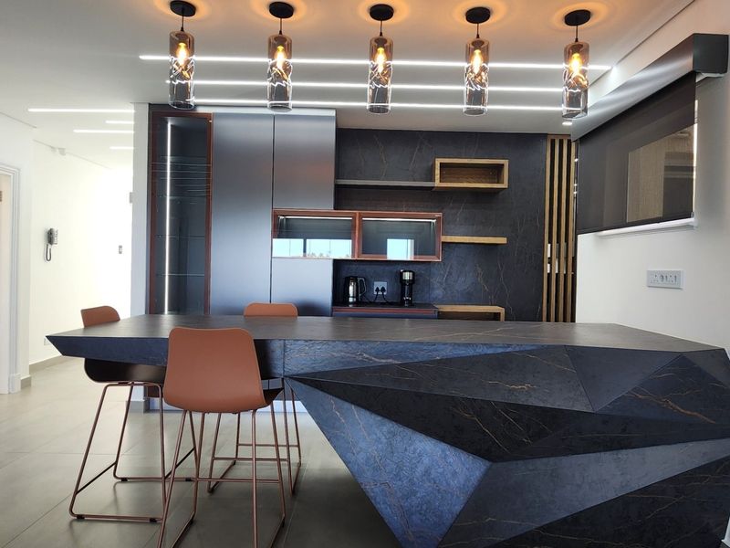 Modern open-plan kitchen featuring a striking geometric stone island, sleek dark cabinetry, integrated shelving, and contemporary pendant lighting in a high-end penthouse setting.
