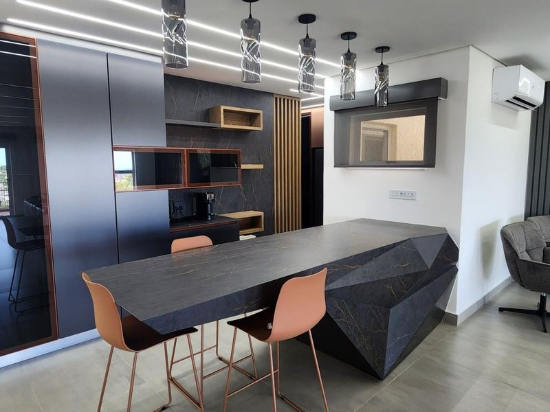 Modern open-plan kitchen featuring a geometric stone-topped island, sleek dark cabinetry, integrated lighting, and contemporary finishes in a sophisticated penthouse setting.