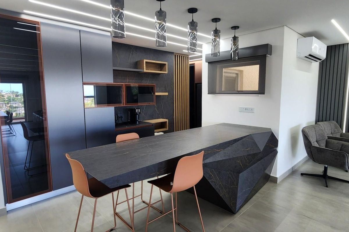 Modern open-plan kitchen featuring a geometric stone-topped island, sleek dark cabinetry, integrated lighting, and contemporary finishes in a sophisticated penthouse setting.