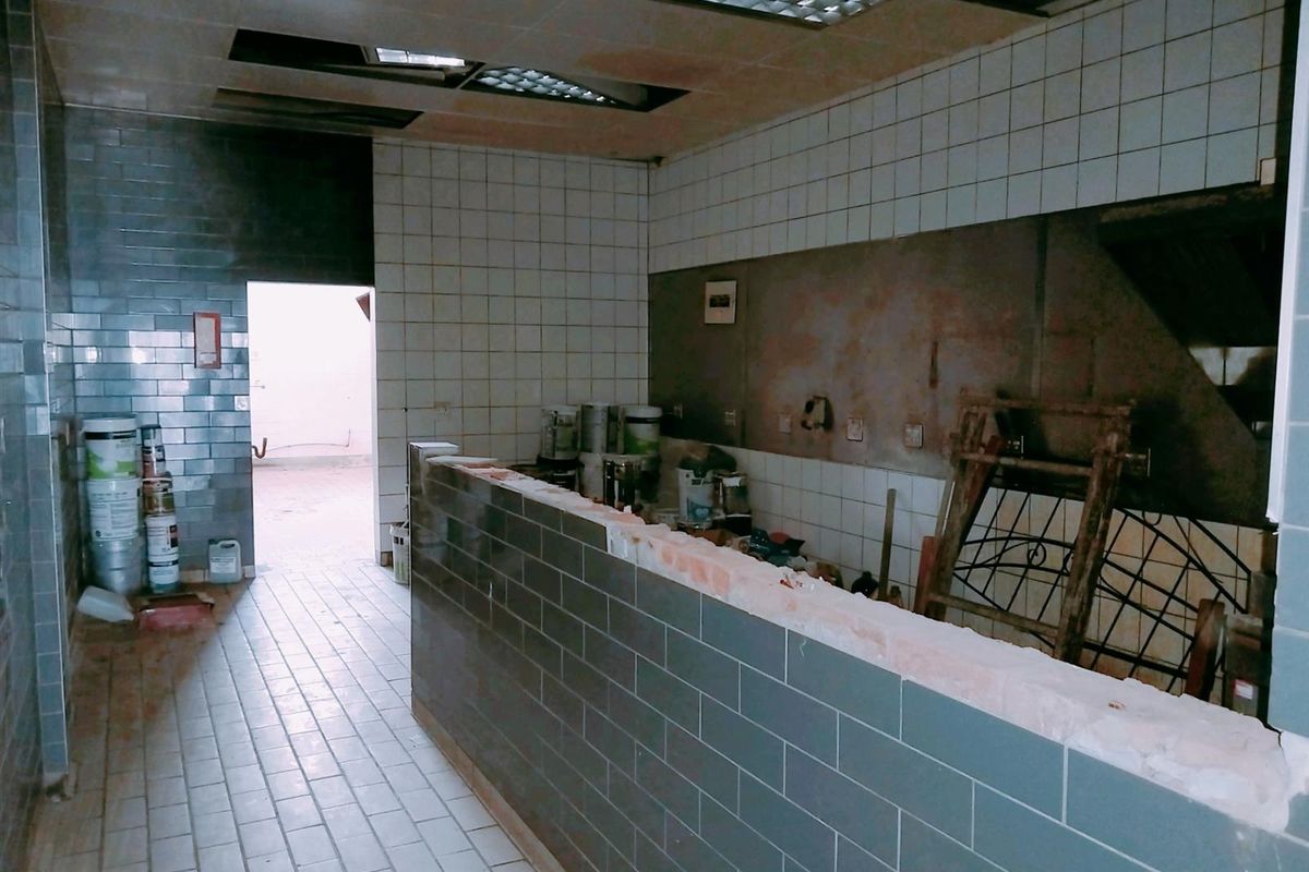 A commercial kitchen space in need of renovation, featuring tiled surfaces, a drop ceiling, and a central service counter.
