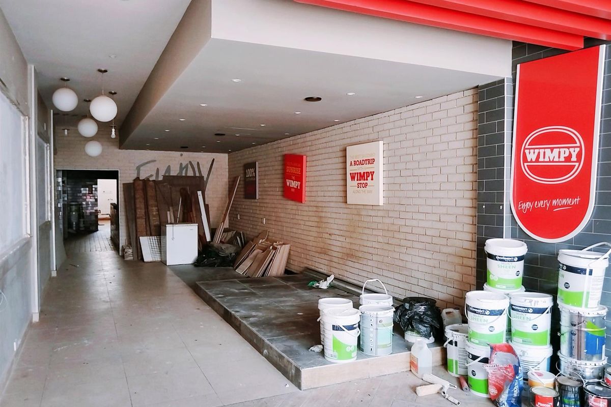 Commercial interior space currently under renovation, featuring a raised platform, exposed brick wall, and recessed lighting, suitable for a restaurant or retail fit-out.