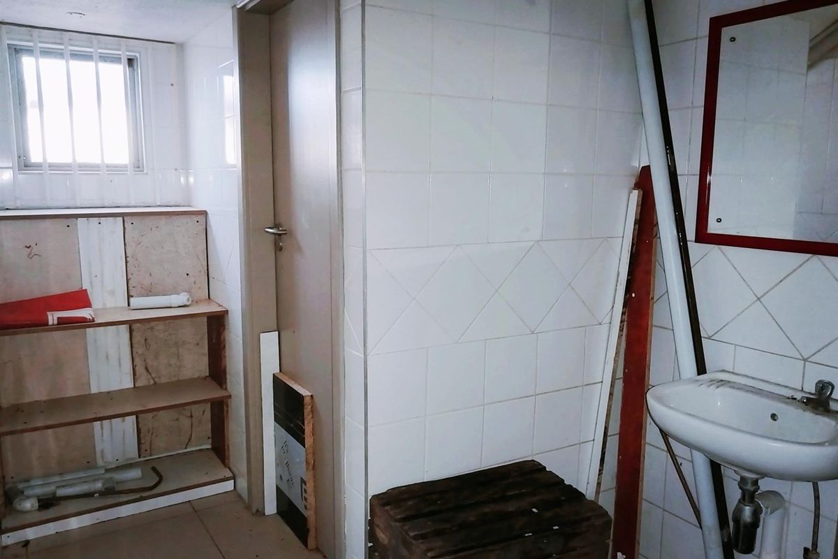 A small, dated bathroom or utility space featuring white wall tiles, a pedestal sink, and built-in shelving, currently in need of renovation.
