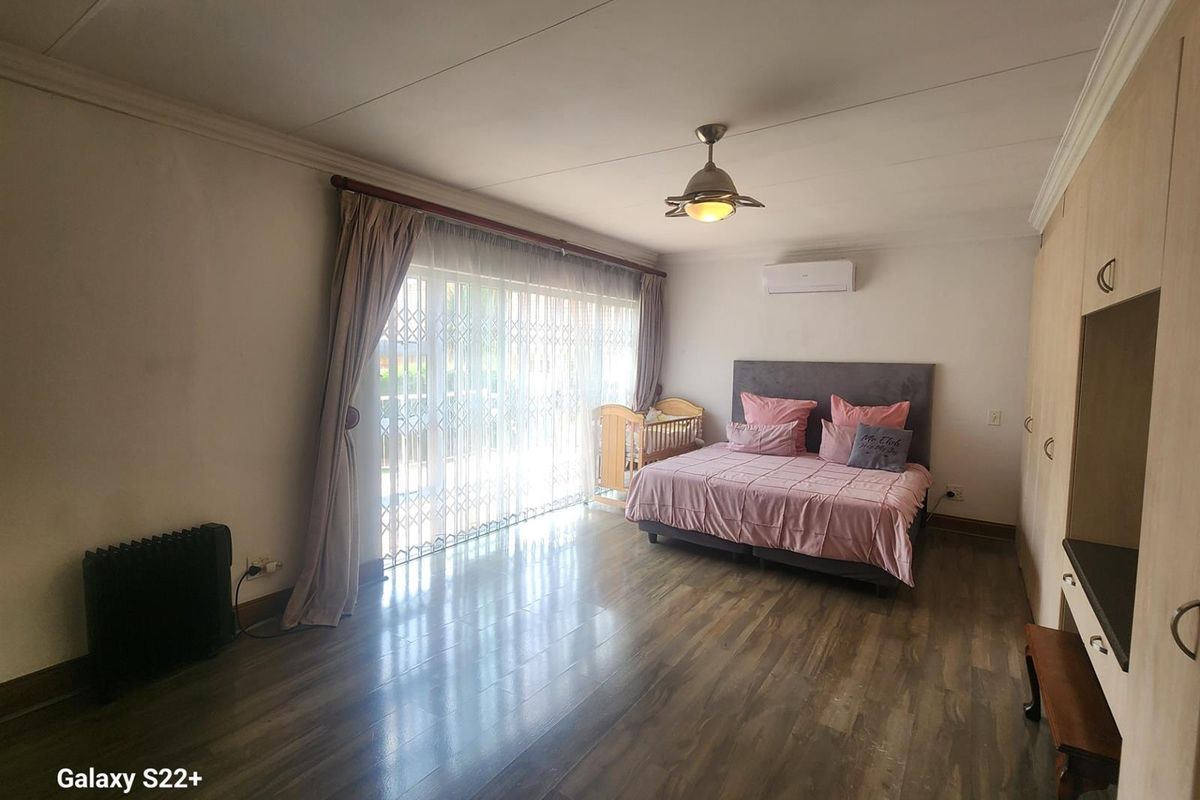 Spacious bedroom featuring wood-look laminate flooring, built-in cabinetry, a ceiling fan, and a wall-mounted air conditioning unit with sliding door access to the exterior.
