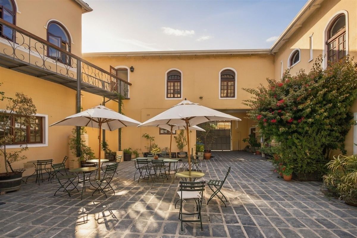 A spacious outdoor courtyard featuring paved flooring, arched windows, and a metal balcony, providing a versatile area for commercial use or outdoor seating.