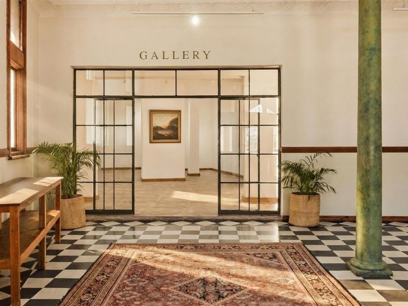 Elegant commercial gallery space featuring classic black and white checkered flooring, decorative column, and large industrial-style steel-framed glass doors.