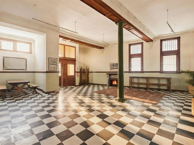 Spacious open-plan commercial area featuring classic checkered flooring, a central structural column, decorative ceiling cornices, and a built-in fireplace.