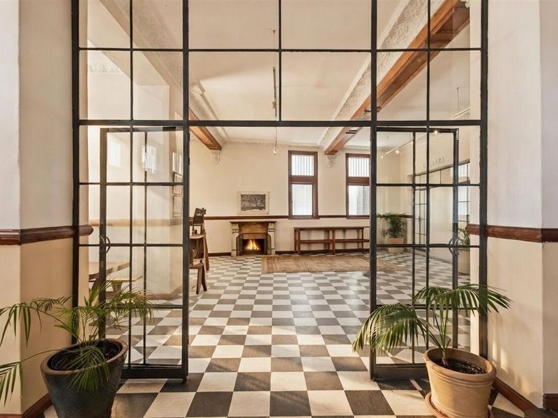 Spacious commercial interior featuring classic checkered flooring, high ceilings with decorative molding, exposed timber beams, and a prominent fireplace, enclosed by industrial-style glass partitions.