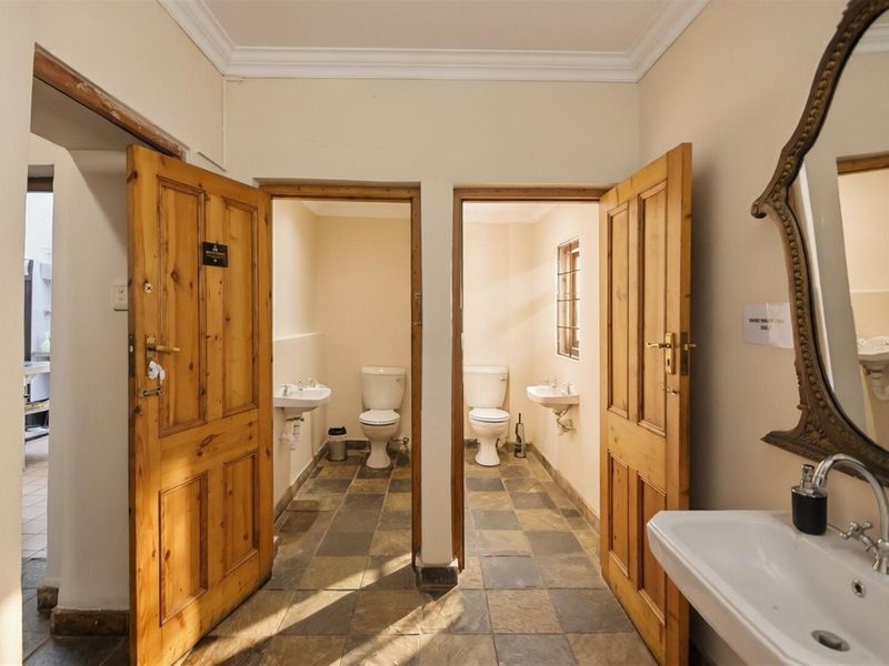 A commercial restroom facility featuring two separate toilet cubicles with tiled flooring, wall-mounted basins, and traditional wooden doors.