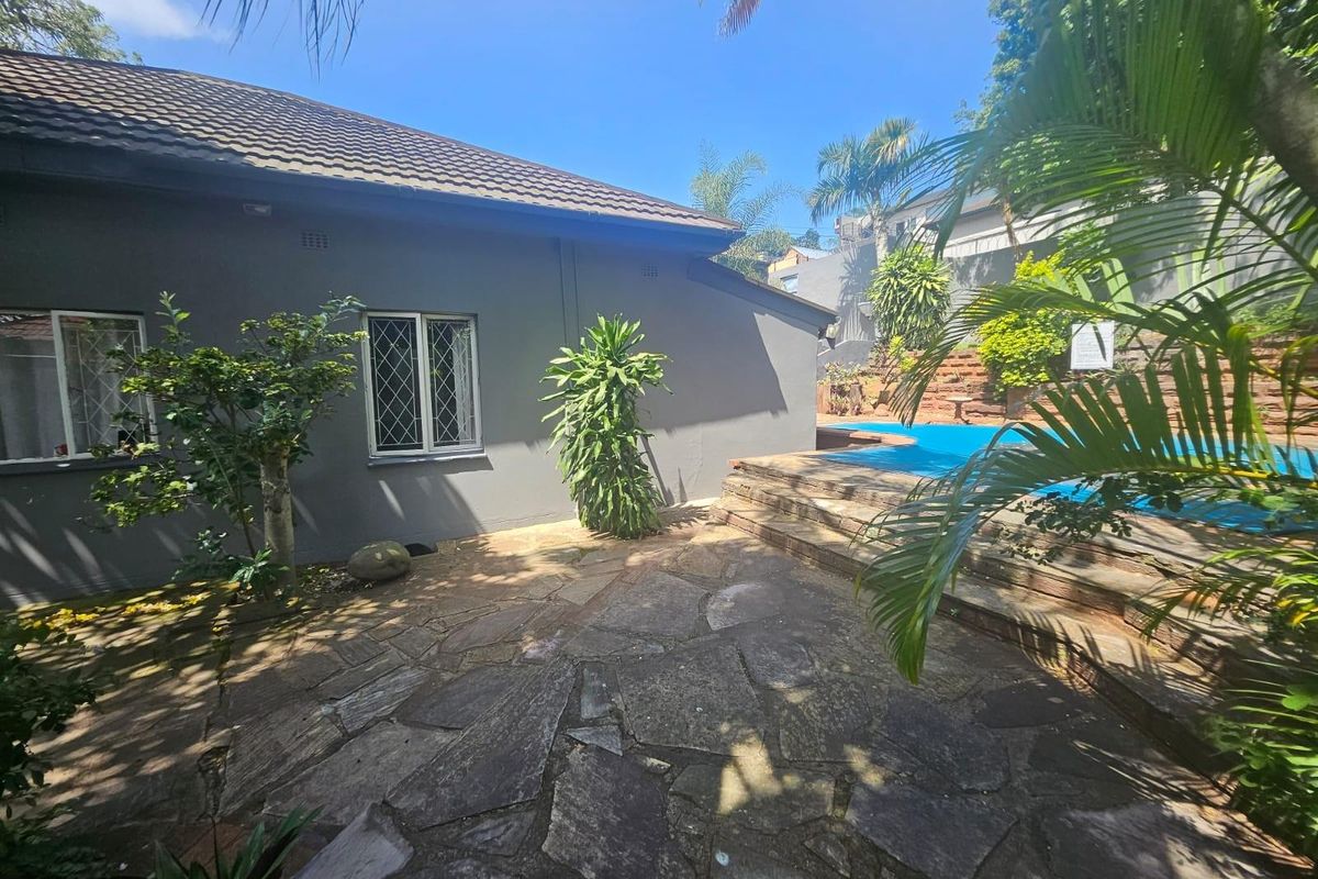 Rear exterior view featuring a paved patio area, swimming pool with stone steps, and landscaped garden surroundings.