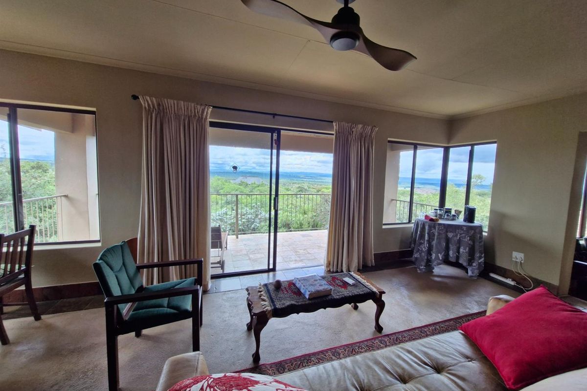 A living room featuring large sliding glass doors that open onto a balcony with scenic landscape views and a ceiling fan.