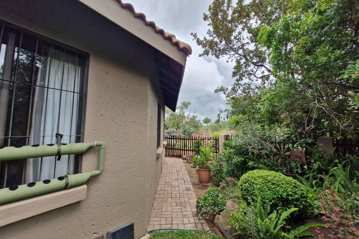 A side exterior view of the property featuring a paved walkway, landscaped garden area, and a secure gate.