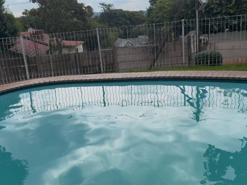 A private swimming pool featuring brick coping and secure metal perimeter fencing, set within a residential garden area.