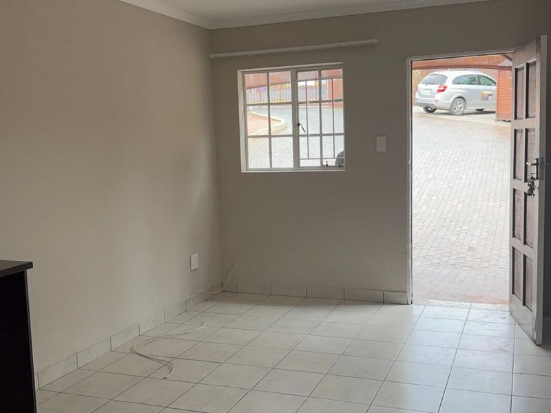 An empty open-plan living area featuring tiled flooring, neutral walls, and direct access to the exterior through a security door.