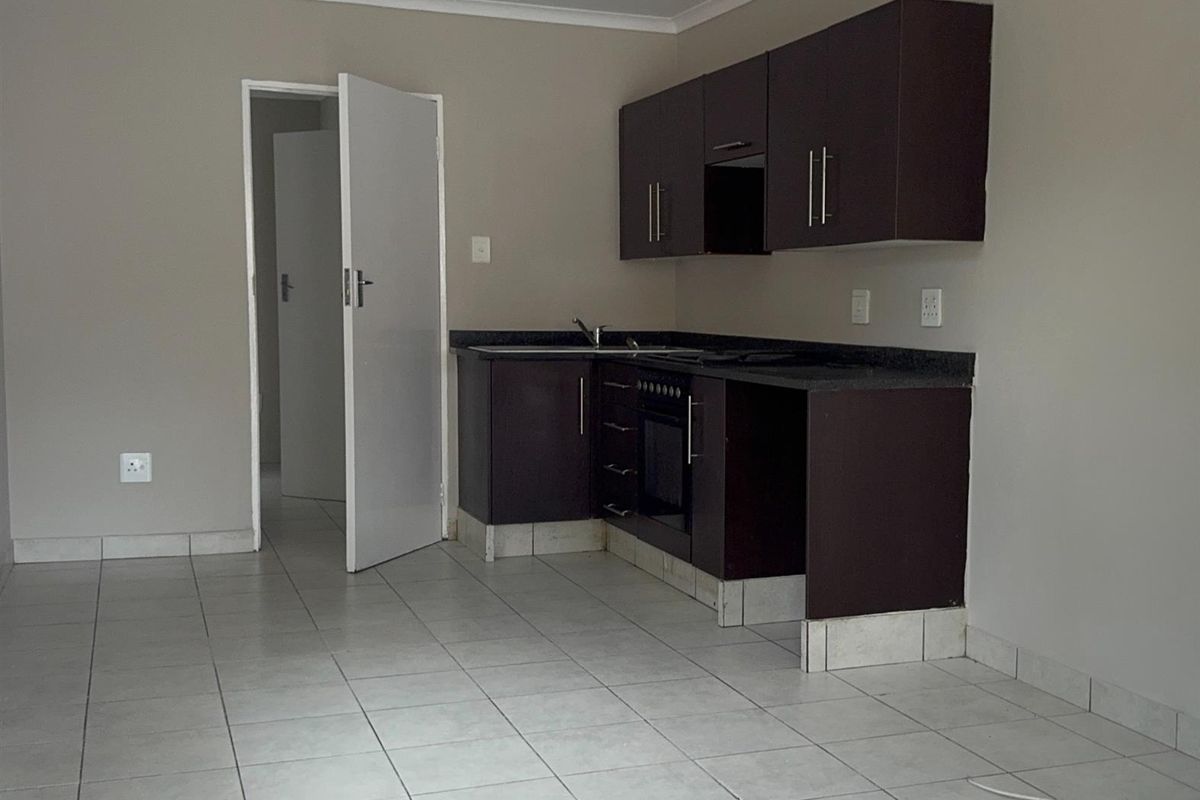 A functional kitchen featuring dark wood cabinetry, built-in oven, hob, and tiled flooring in an open-plan layout.