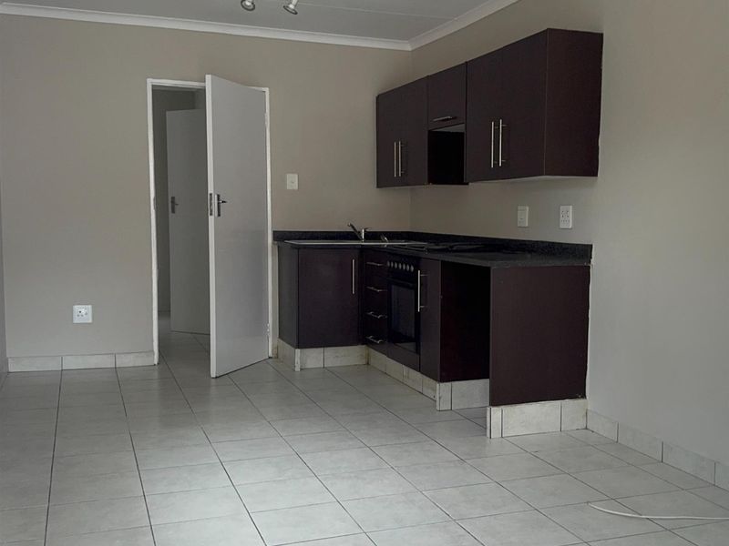 A functional kitchen featuring dark wood cabinetry, built-in oven, hob, and tiled flooring in an open-plan layout.
