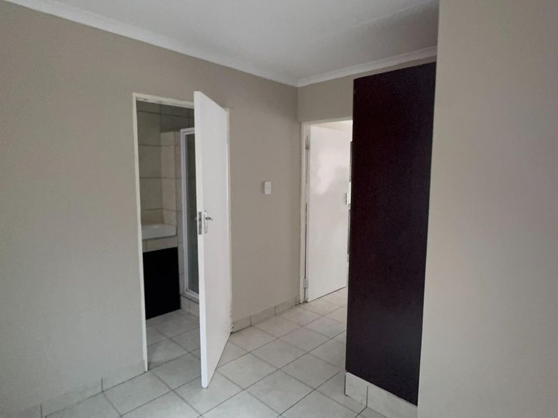 A clean, neutral-toned hallway featuring tiled flooring, a built-in cupboard, and access to adjacent rooms, including a bathroom.