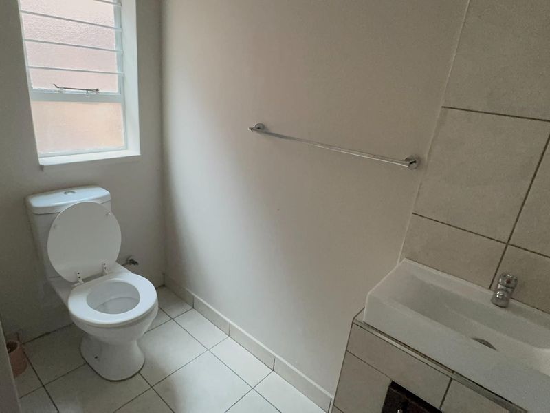 A functional bathroom featuring a toilet, vanity basin, tiled flooring, and a tiled wall splashback, providing a clean and practical space.