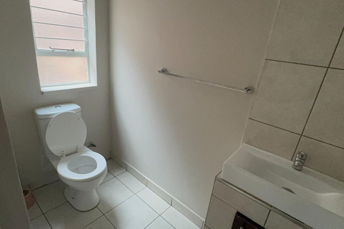 A functional bathroom featuring a toilet, vanity basin, tiled flooring, and a tiled wall splashback, providing a clean and practical space.