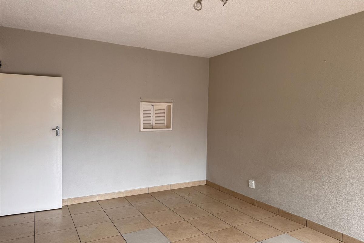An empty living area featuring neutral wall tones, tiled flooring with some mismatched tiles, and a ceiling-mounted spotlight fixture.