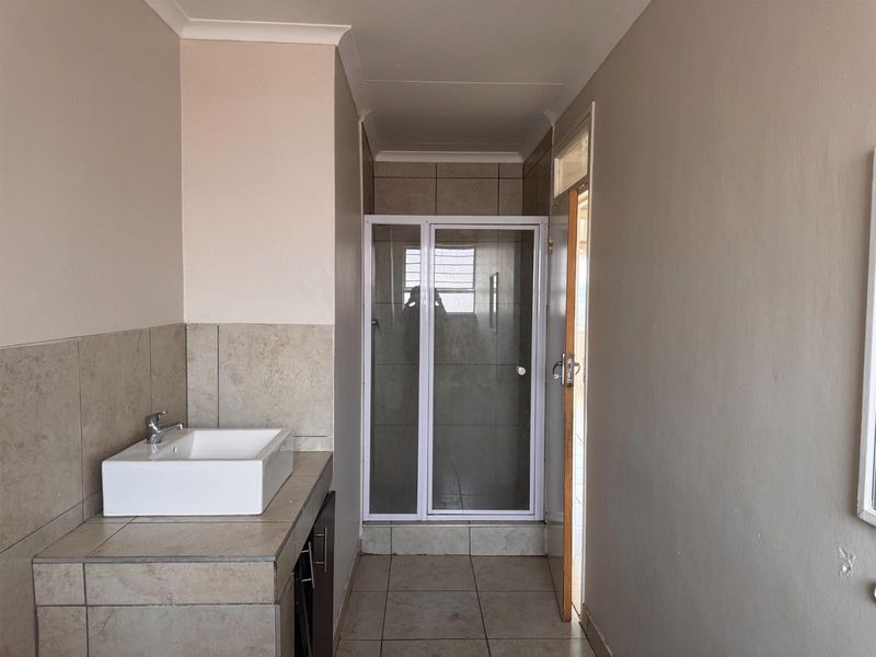 A functional bathroom featuring a tiled vanity with a basin, a shower enclosure, and neutral wall finishes.