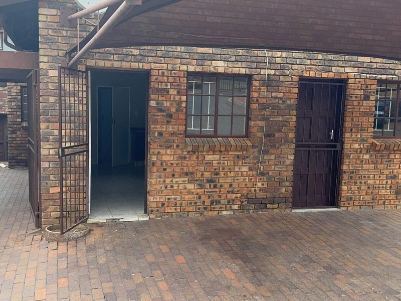 Exterior view of an apartment entrance featuring face brick construction, a paved driveway, and a covered carport area with security gates.