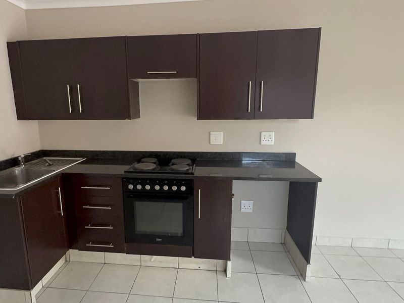 A functional kitchen featuring dark wood cabinetry, granite countertops, a built-in oven with electric hob, and tiled flooring.