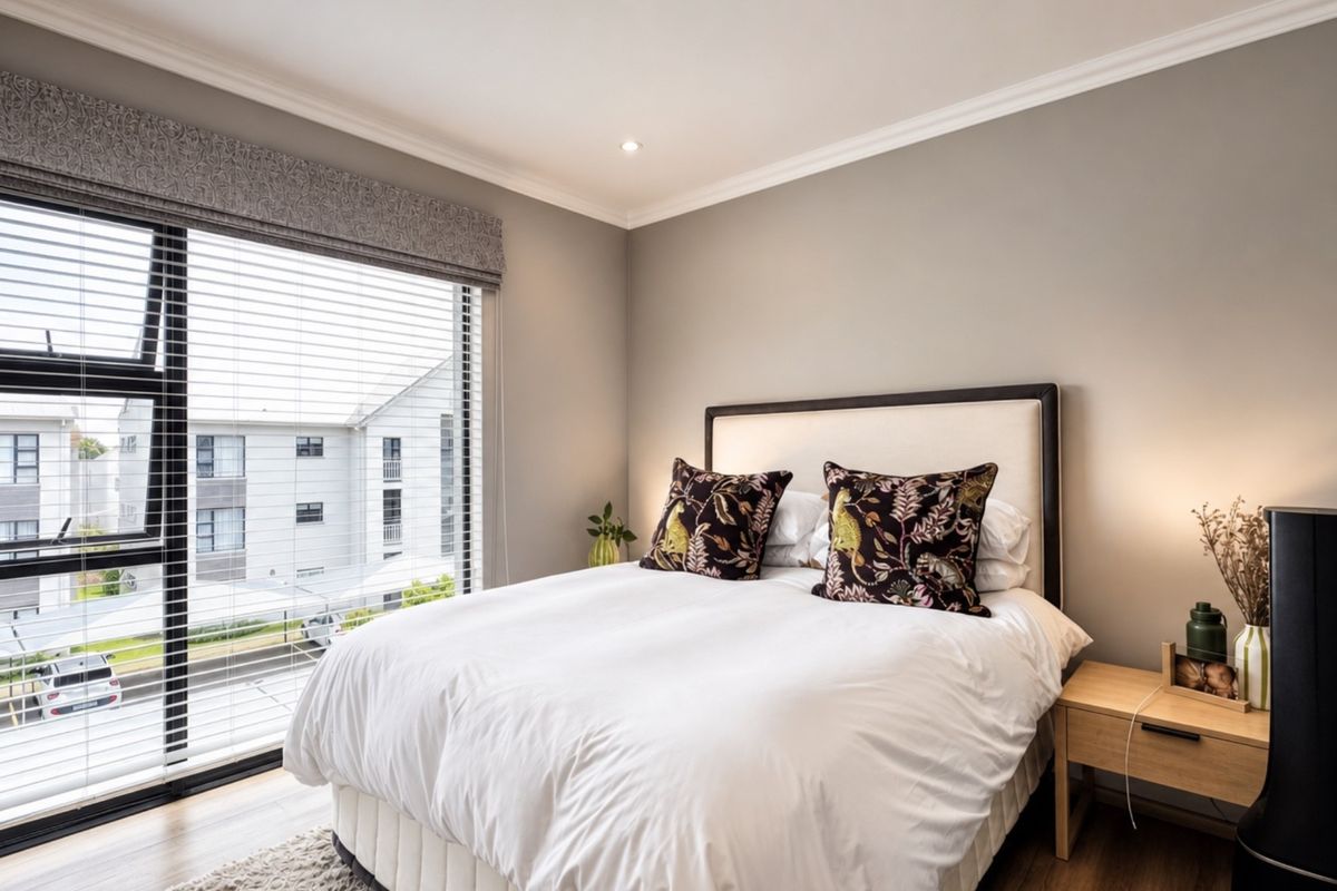 A well-maintained bedroom featuring neutral wall tones, laminate flooring, and a large window with venetian blinds providing natural light and exterior views.