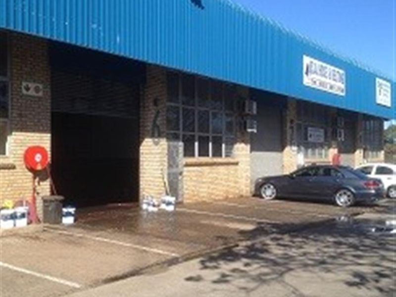 Industrial warehouse facility featuring a blue corrugated metal roof, brick facade, and large roller shutter door access.