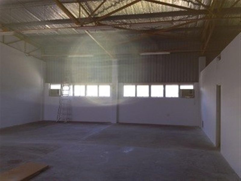 Spacious industrial warehouse interior featuring high exposed steel truss ceilings, concrete flooring, and multiple windows providing natural light.