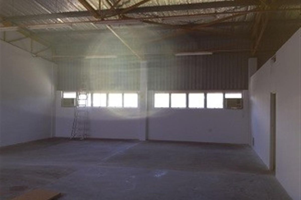 Spacious industrial warehouse interior featuring high exposed steel truss ceilings, concrete flooring, and multiple windows providing natural light.