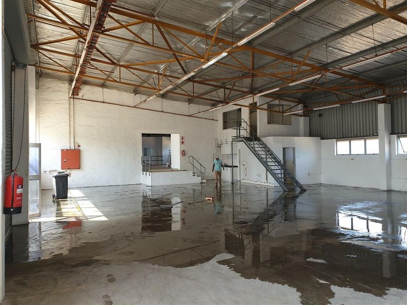 Spacious industrial warehouse featuring high ceilings with exposed steel trusses, concrete flooring, and an integrated mezzanine level with staircase access.