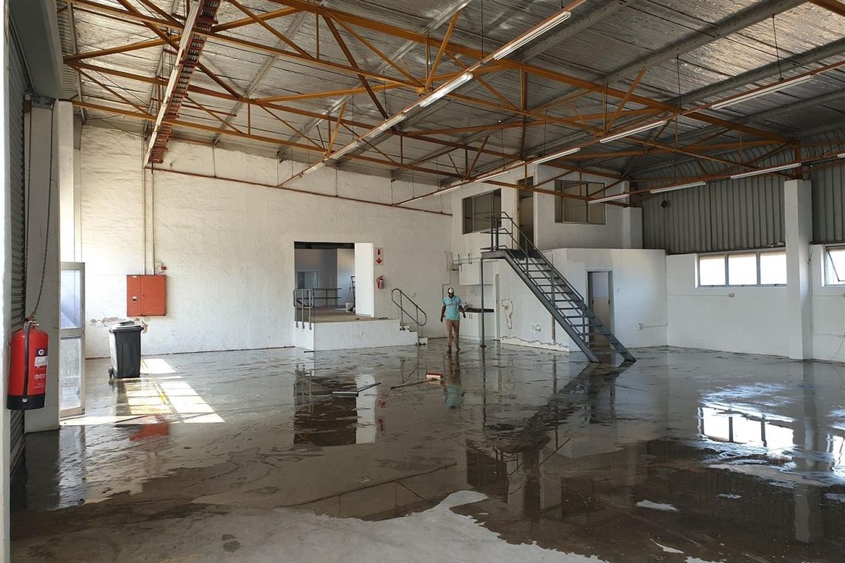 Spacious industrial warehouse featuring high ceilings with exposed steel trusses, concrete flooring, and an integrated mezzanine level with staircase access.