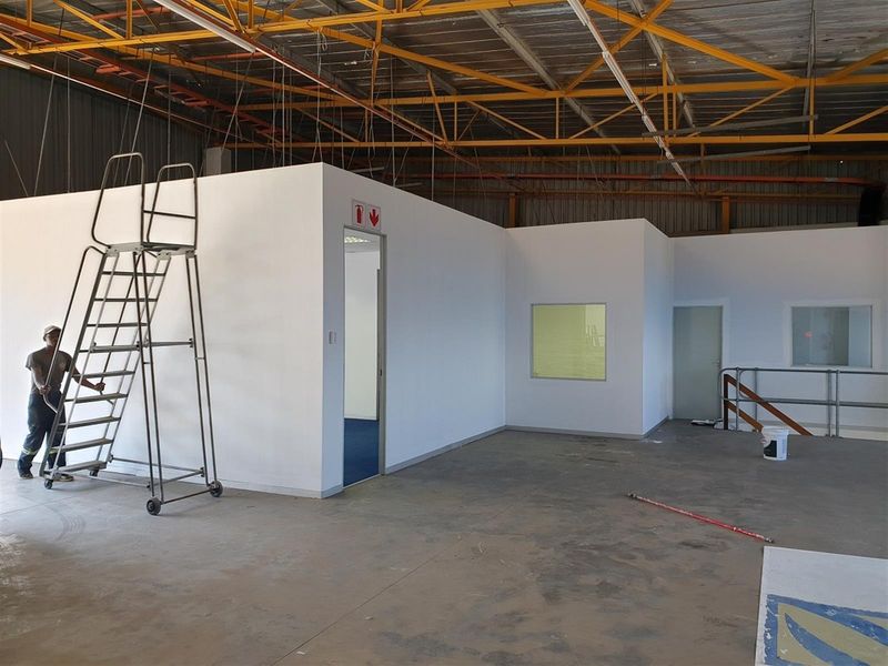 Industrial warehouse space featuring a newly constructed internal office block with white partition walls, metal roof trusses, and concrete flooring.