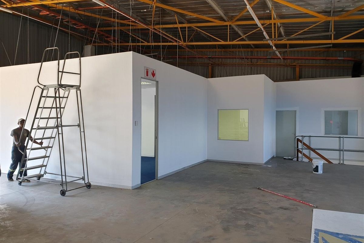 Industrial warehouse space featuring a newly constructed internal office block with white partition walls, metal roof trusses, and concrete flooring.