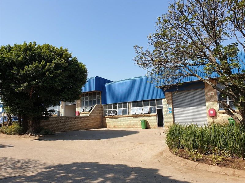 Industrial property exterior featuring a brick facade, blue corrugated metal roof, roller shutter door, and paved driveway access.