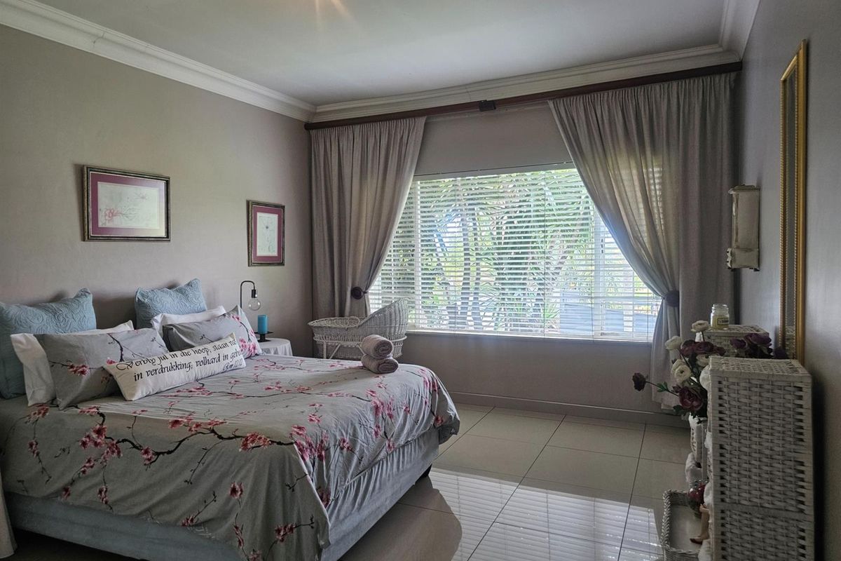 A well-maintained bedroom featuring neutral wall tones, large windows with fitted curtains and blinds, and polished floor tiles.